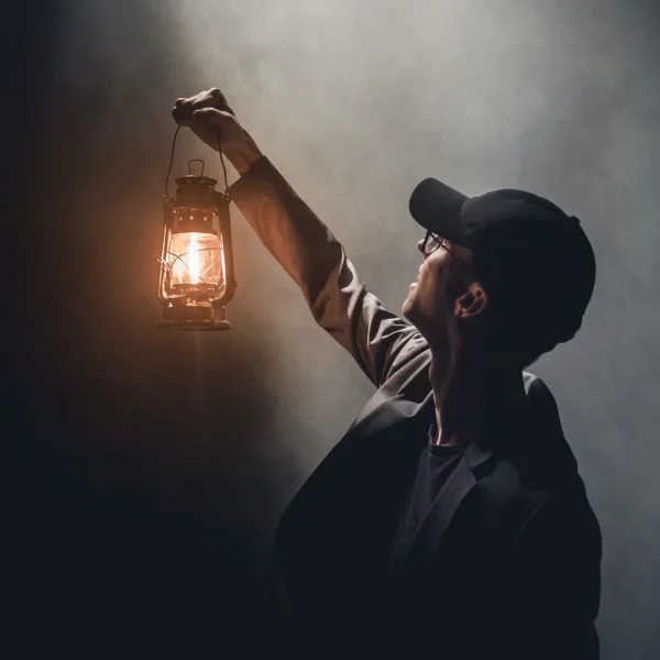 A man holding up a paraffin lamp in dark and misty surroundings, looking up