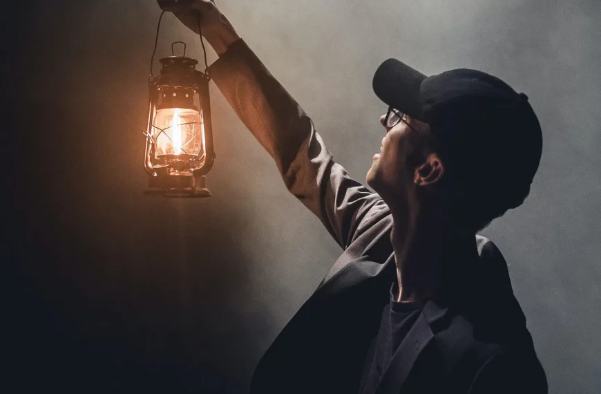 A man holding up a paraffin lamp in dark and misty surroundings, looking up