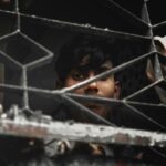 Boy standing behind metal fence