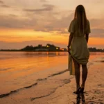 Woman standing on the beach, watching the sunset