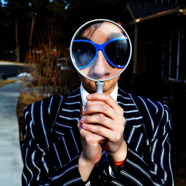 A man holding a magnifying glass in front of his head while facing the photographer