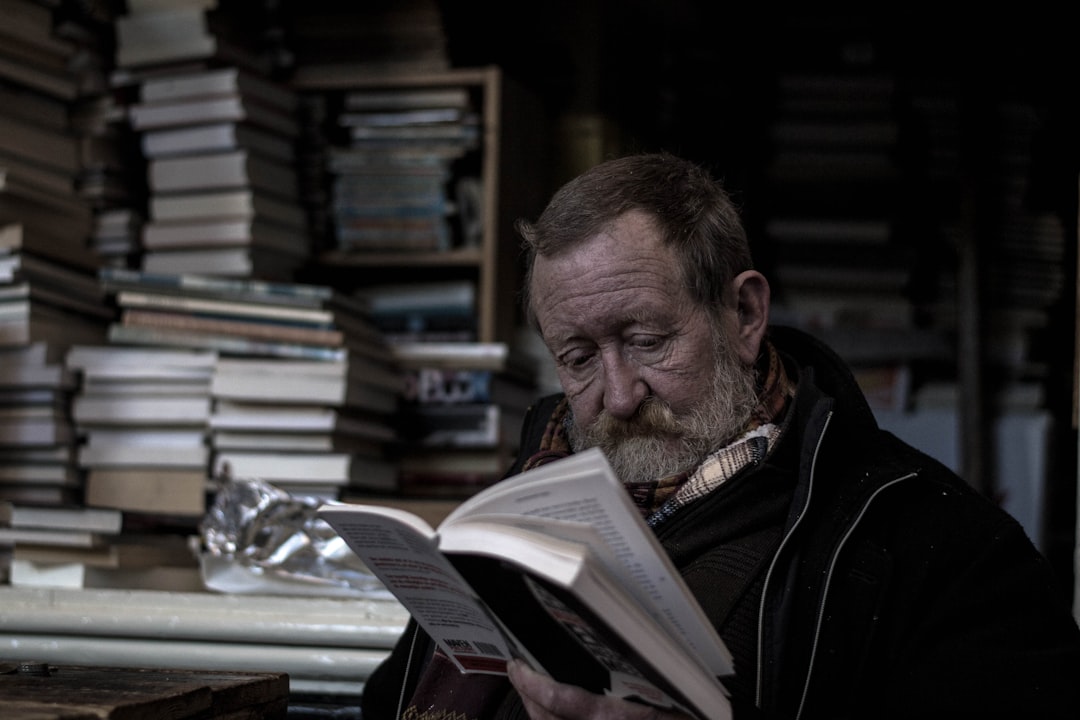A man is reading a book, with piles of other books behind him