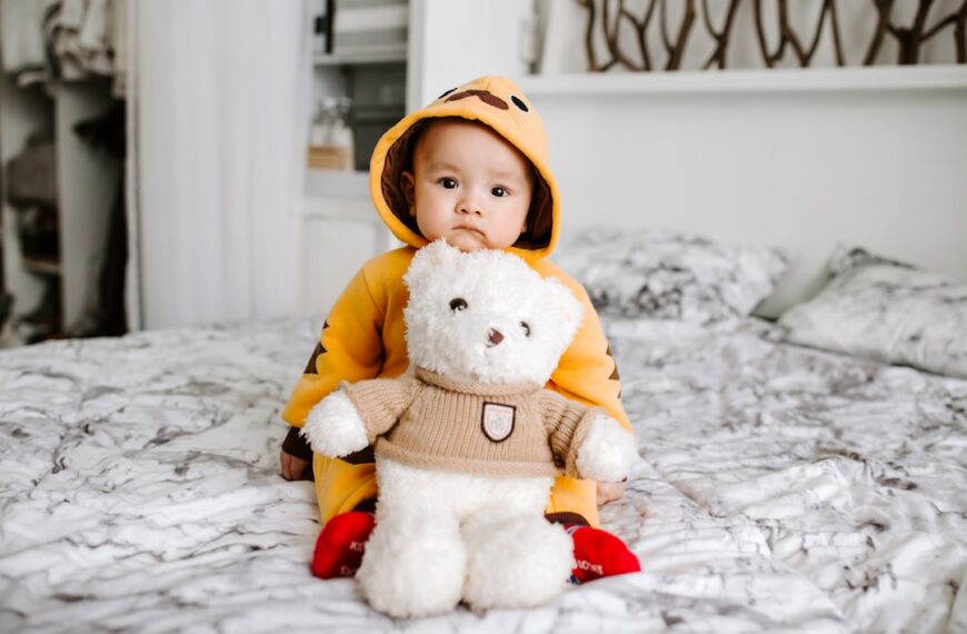 A child sitting on a large bed, holding a big teddy bear