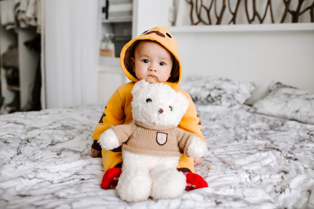 A child sitting on a large bed, holding a big teddy bear