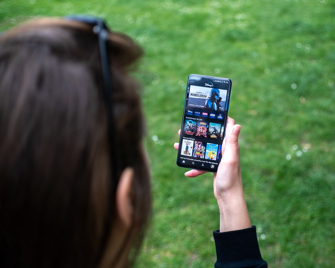 A man is looking at a smartphone, while standing on the grass