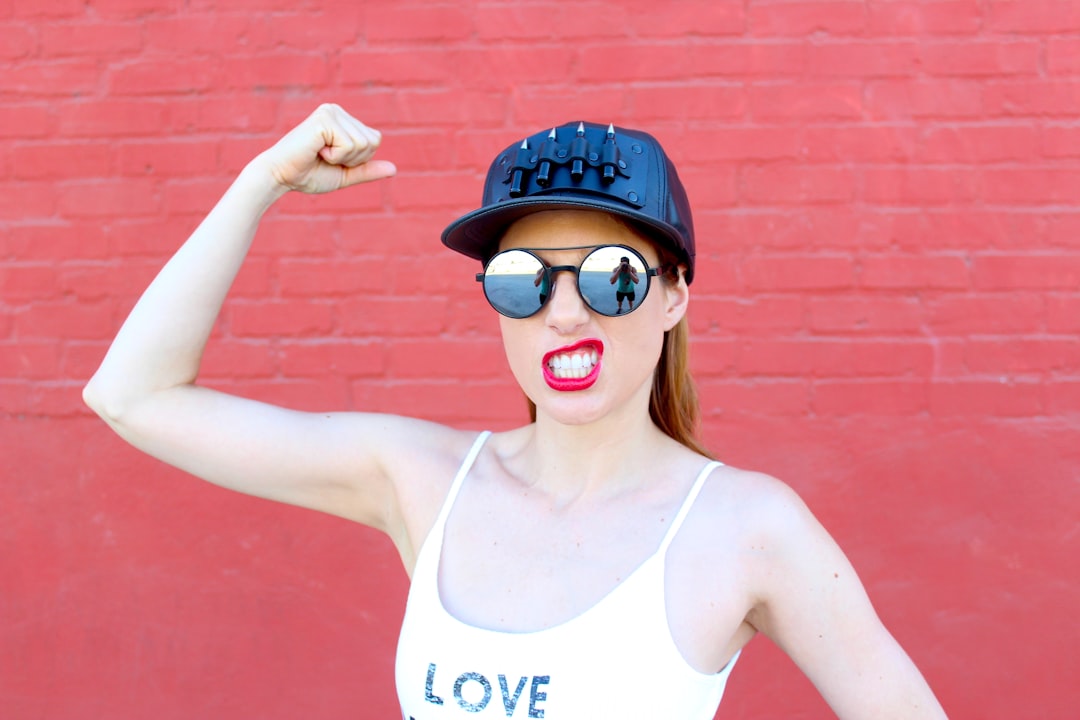 Woman with a cap, sunglasses, and a top with the word "Love" written on it, holding her arm up to show her muscles